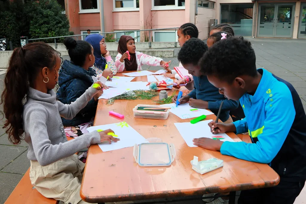 Kinder sitzen am Maltisch und unterhalten sich.
